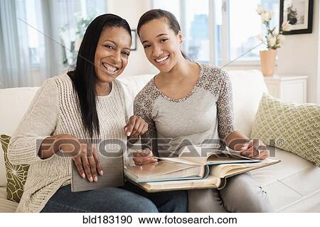 Stock Image - Mother and daughter looking at photo album on sofa. Fotosearch
