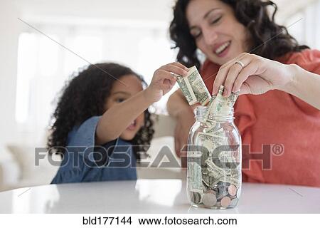 Picture - Mother and daughter saving money in jar. Fotosearch