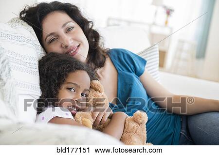 Stock Image - Mother and daughter sitting on sofa. Fotosearch