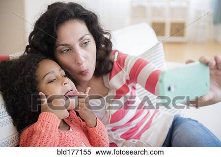Stock Photography - Mother and daughter taking selfie on sofa. Fotosearch