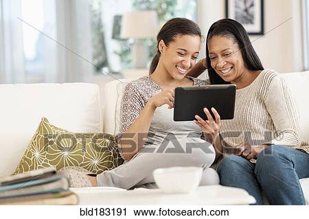 Stock Image - Mother and daughter using digital tablet on sofa. Fotosearch