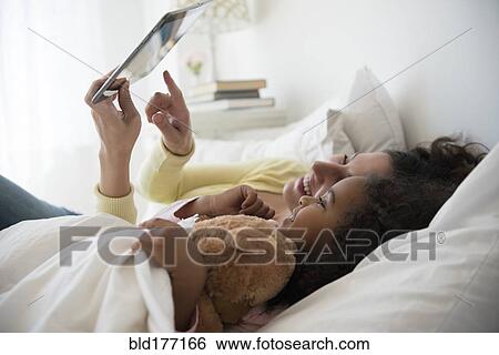 Stock Photograph - Mother and daughter using digital tablet in bed. Fotosearch