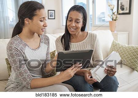 Stock Photography - Mother and daughter using digital tablet on sofa. Fotosearch