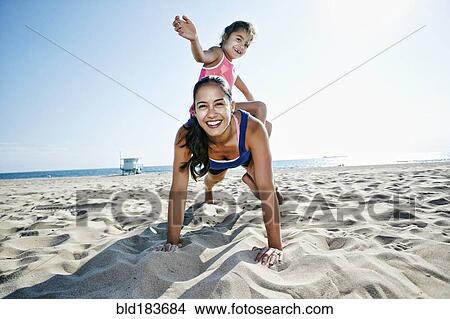 Picture - Mother doing push-ups with daughter at beach. Fotosearch