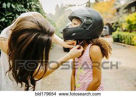 Picture - Mother fastening helmet on daughter. Fotosearch
