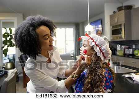Stock Image - Mother painting face or daughter for Halloween. Fotosearch