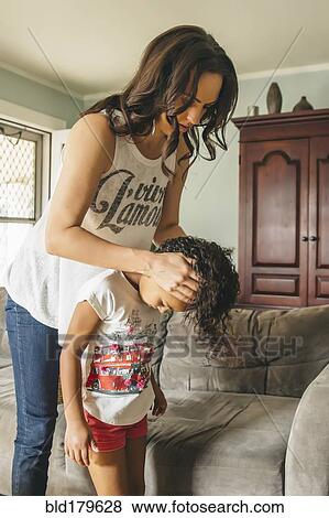 Stock Photo - Mother styling hair for daughter in living room. Fotosearch