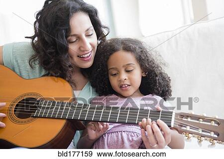 Stock Photo - Mother teaching daughter to play guitar. Fotosearch