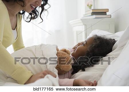 Stock Photography - Mother tucking daughter into bed. Fotosearch