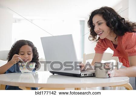 Stock Image - Mother using laptop at breakfast with daughter. Fotosearch
