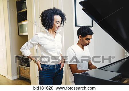 Stock Image - Mother watching son play piano. Fotosearch