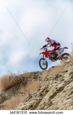 Stock Image - Motorcyclist riding dirt bike on hillside. Fotosearch