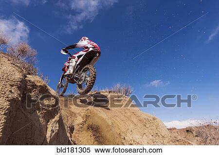 Stock Photography - Motorcyclist riding dirt bike on hillside. Fotosearch