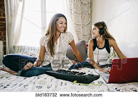 Stock Image - Native American mother and daughter playing keyboard on bed. Fotosearch