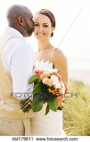 Stock Image - Newlywed couple kissing in grass. Fotosearch