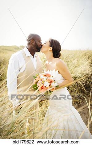 Newlywed couple kissing in grass View Large Photo Image Stock Image - Newlywed couple kissing in grass. Fotosearch