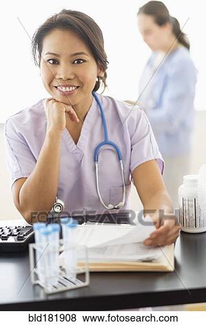 Stock Photo - Nurse smiling at desk in hospital. Fotosearch