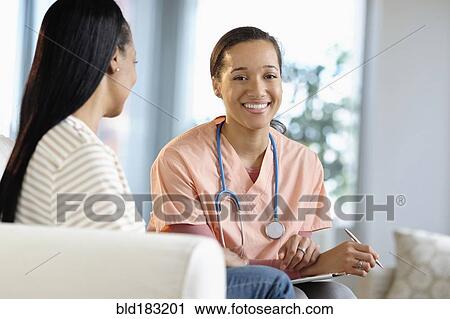 Stock Image - Nurse smiling with patient in living room. Fotosearch