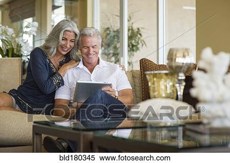 Stock Photography - Older Caucasian couple using digital tablet on sofa. Fotosearch