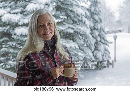 Stock Photograph - Older Caucasian woman drinking coffee on snowy patio. Fotosearch