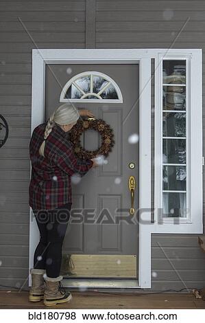 Stock Photo - Older Caucasian woman hanging wreath on front door. Fotosearch