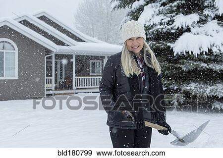Stock Photo - Older Caucasian woman shoveling snow in front yard. Fotosearch