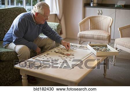Stock Image - Older man on sofa solving jigsaw puzzle. Fotosearch