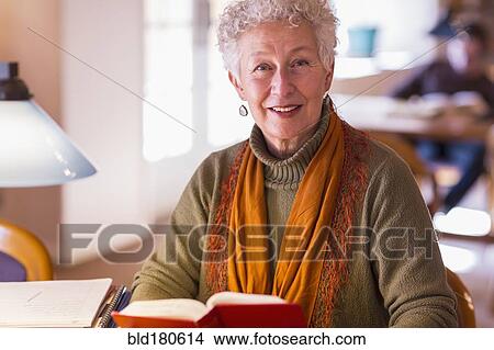 Picture - Older mixed race woman holding book in library. Fotosearch