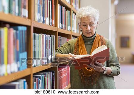 Stock Image - Older mixed race woman reading book in library. Fotosearch