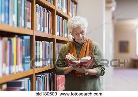 Stock Photo - Older mixed race woman reading book in library. Fotosearch