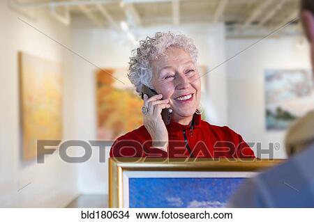 Picture - Older mixed race woman using cell phone in art gallery. Fotosearch