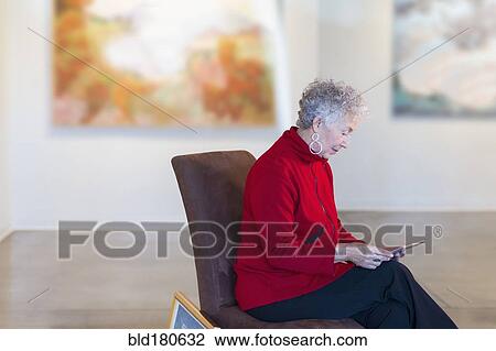 Stock Image - Older mixed race woman using digital tablet in art gallery. Fotosearch