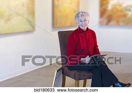 Stock Image - Older mixed race woman using digital tablet in art gallery. Fotosearch