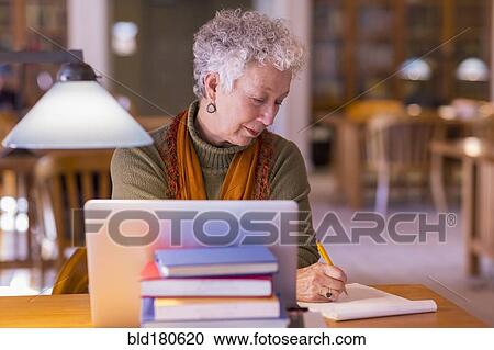 Stock Image - Older mixed race woman using laptop in library. Fotosearch