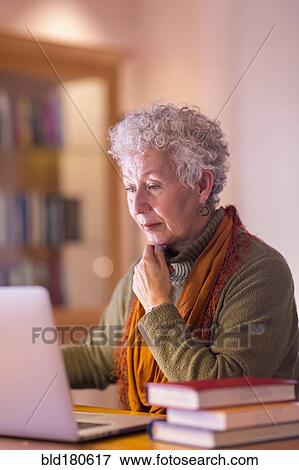 Stock Photo - Older mixed race woman using laptop in library. Fotosearch