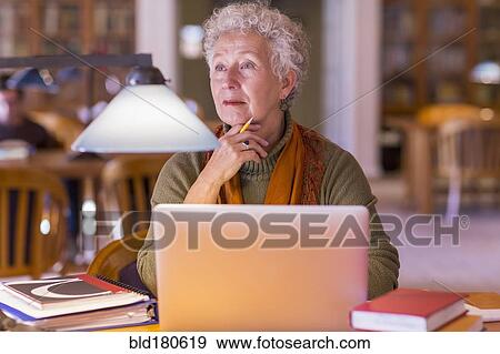 Stock Photo - Older mixed race woman using laptop in library. Fotosearch
