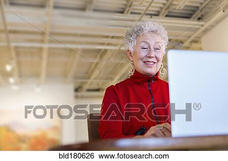 Stock Photograph - Older mixed race woman using laptop in art gallery. Fotosearch