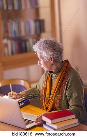 Stock Photograph - Older mixed race woman writing in library. Fotosearch