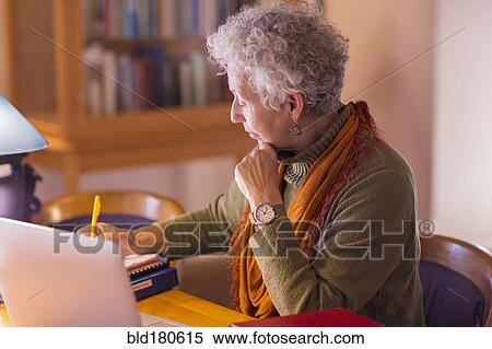 Stock Photography - Older mixed race woman writing in library. Fotosearch