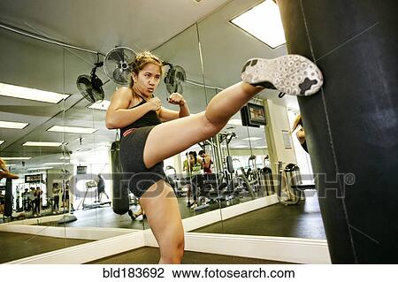 Stock Image - Pacific Islander woman kicking punching bag in gymnasium. Fotosearch
