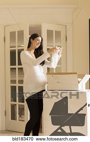 Stock Image - Pregnant Caucasian woman admiring baby clothing. Fotosearch