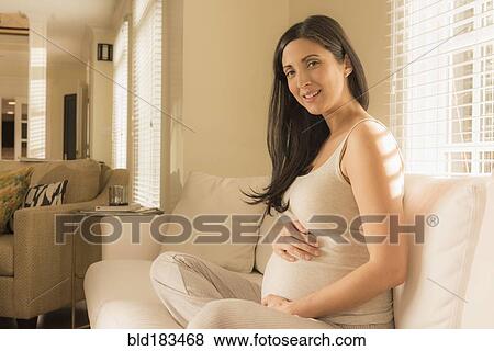 Stock Photo - Pregnant Caucasian woman sitting on sofa. Fotosearch
