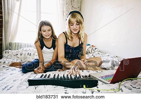 Stock Image - Sisters playing keyboard on bed. Fotosearch