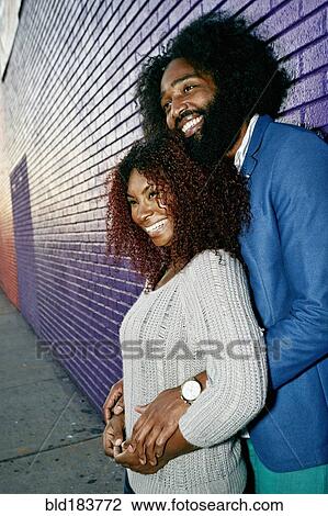 Stock Image - Smiling couple hugging outdoors near purple wall. Fotosearch