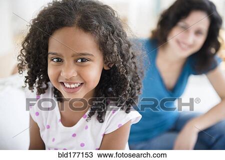 Stock Image - Smiling girl and mother on sofa. Fotosearch