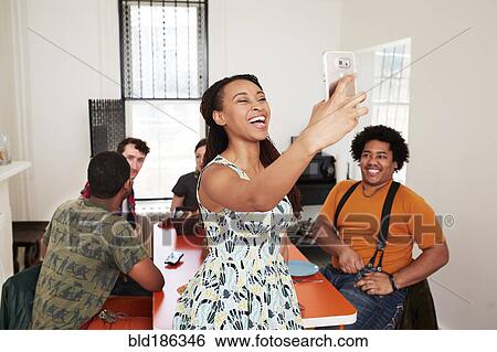 Stock Photograph - Smiling woman taking selfie with friends. Fotosearch
