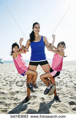 Stock Image - Strong mother lifting daughters at beach. Fotosearch
