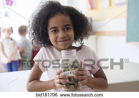 Stock Photograph - Student holding savings jar in classroom. Fotosearch