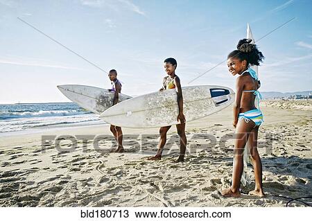 Stock Image - Three generations of Black women carrying surfboards on beach. Fotosearch