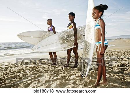 Stock Photo - Three generations of Black women carrying surfboard on beach. Fotosearch